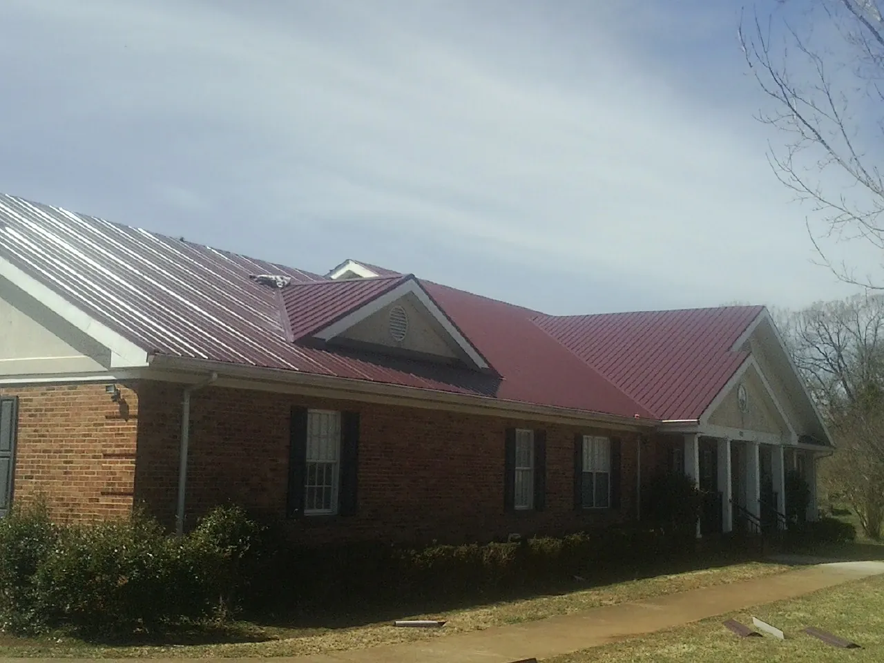 Red metal roof with gabled entries on a long brick building, from a Hail Damage Roof Repair job in Fort Plain