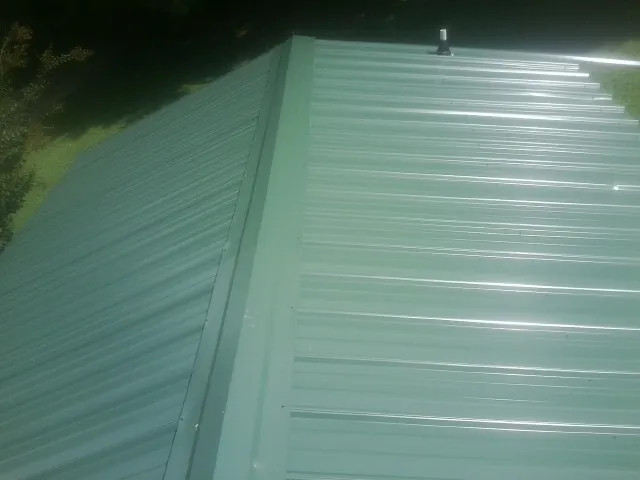 New green metal panels meeting at the ridge of a roof — Flat Roof Repair work by our crew in Fort Plain