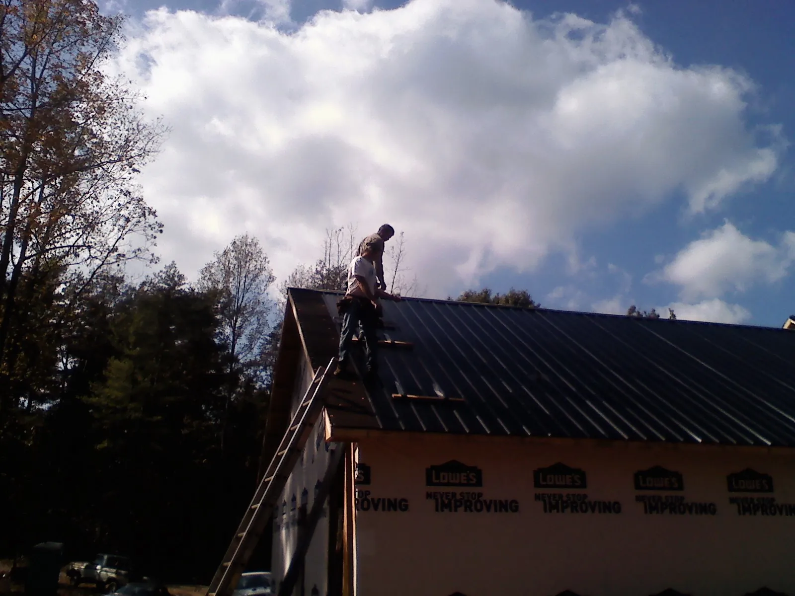 Roofer fastening dark metal panels high against a cloudy sky, from a Roof Inspection job in Fort Plain