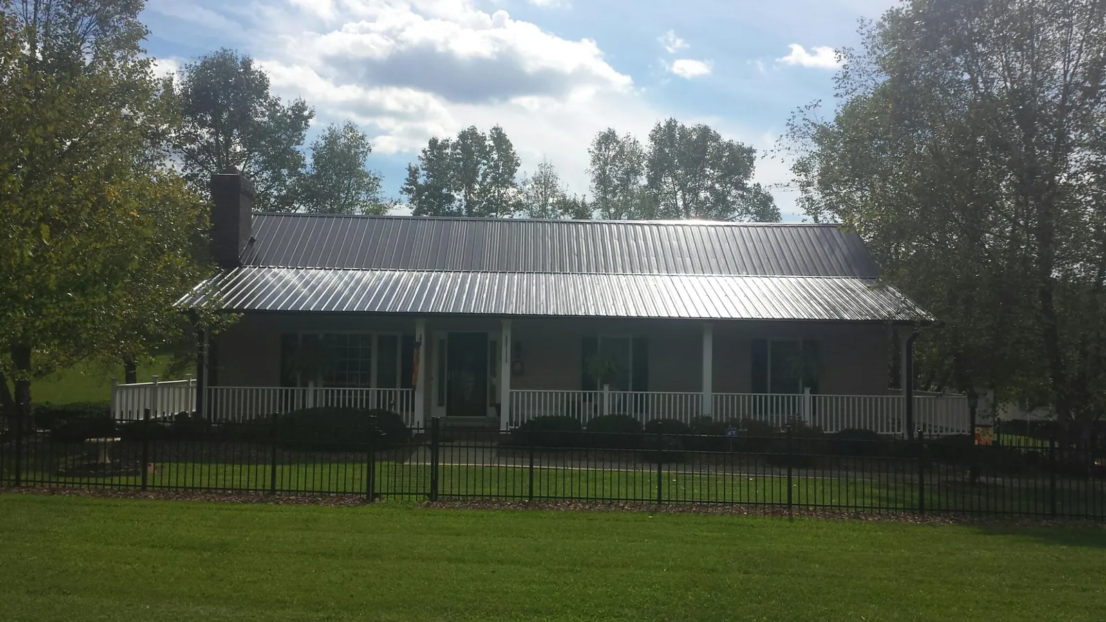 Gray metal roof on a brick ranch with a full width front porch — Gutter Guard Installation work by our crew in Fort Plain