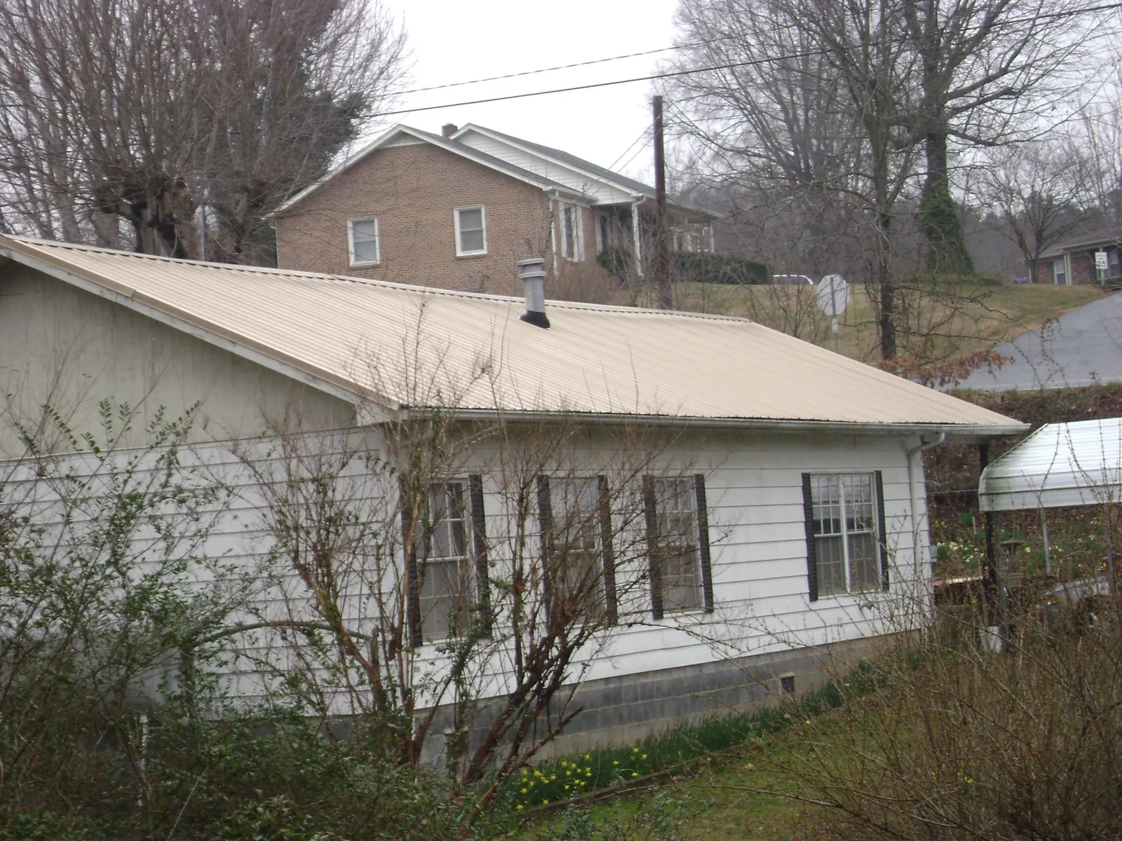 Tan metal roof on a white sided house set into a hillside — Commercial Roofing by Roofing Brothers in Fort Plain